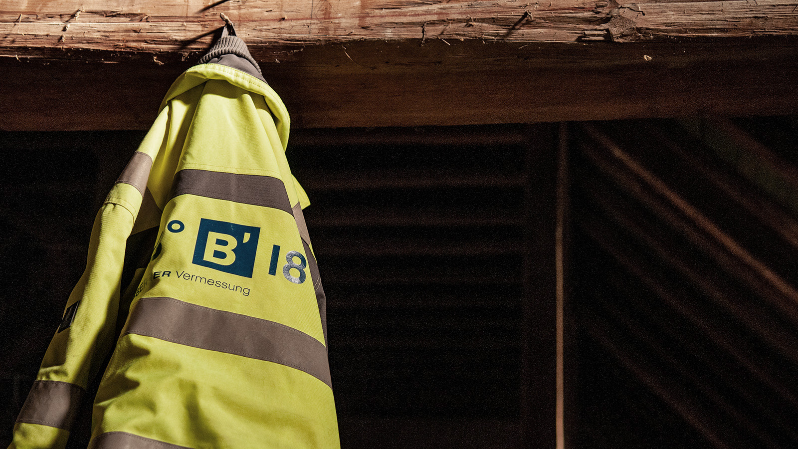 Eine blaugelbe Arbeitsjacke von Bogensberger hängt auf einem Holzbalken